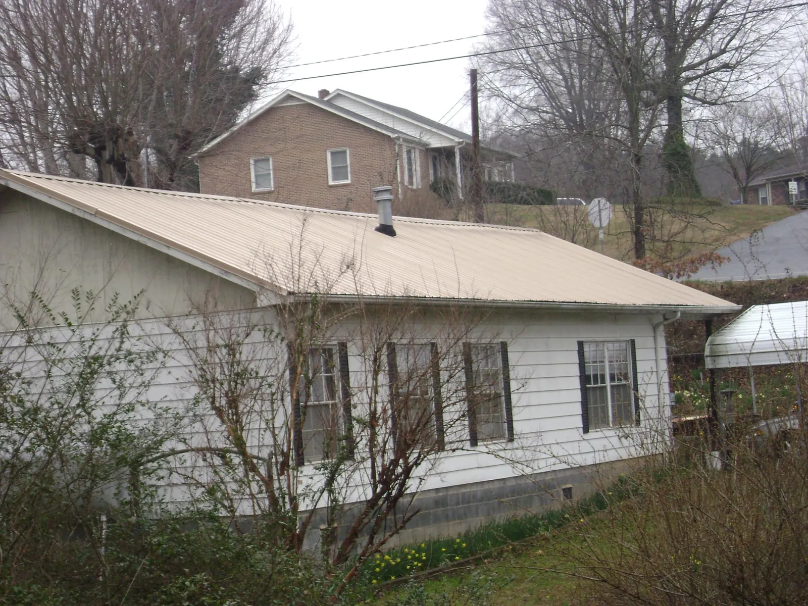 Tan metal roof on a white sided house set into a hillside — Commercial Roofing by Roofing Brothers in Unionville